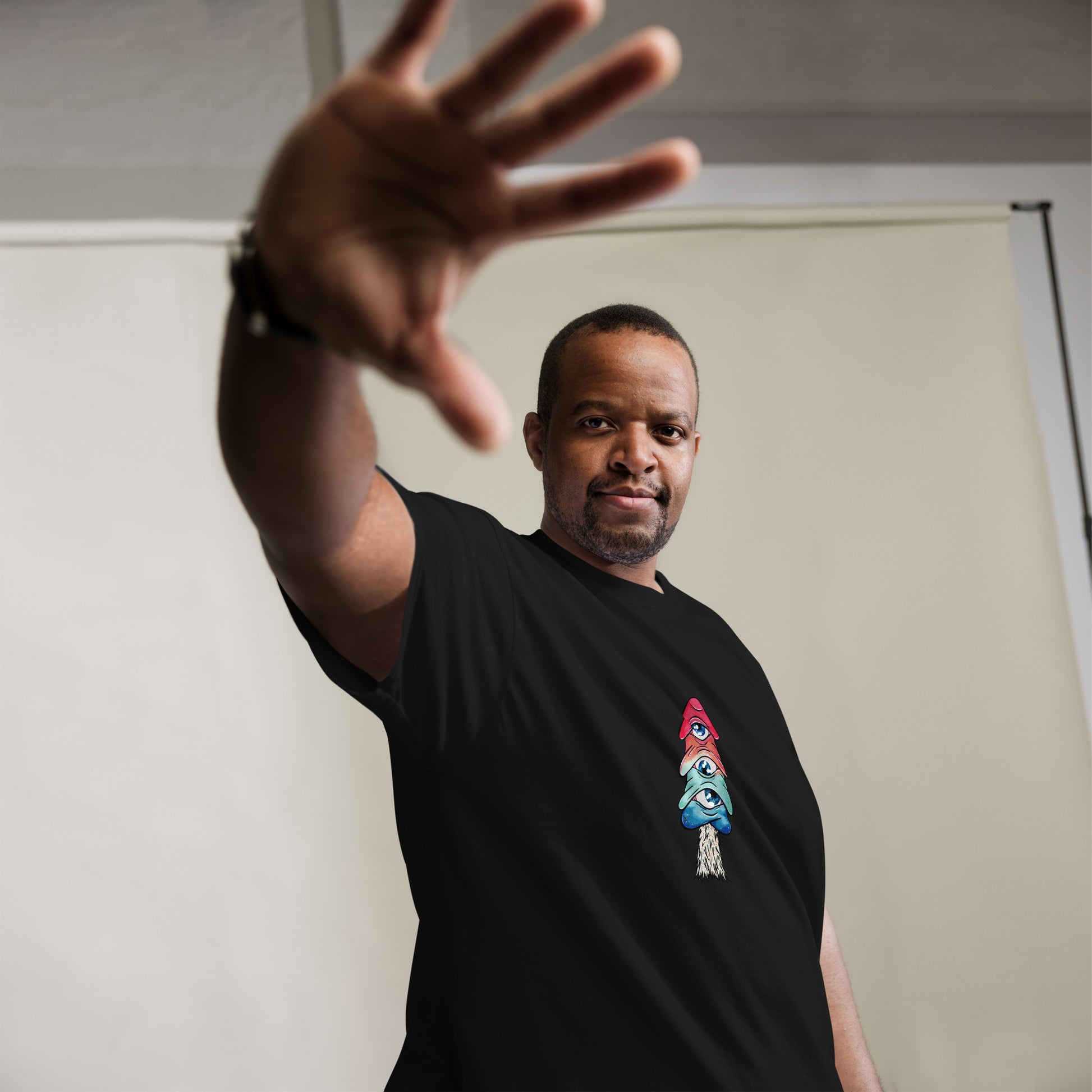 male model wears black crew neck tshirt mushroom with 3 eyes in pink green and blue side view